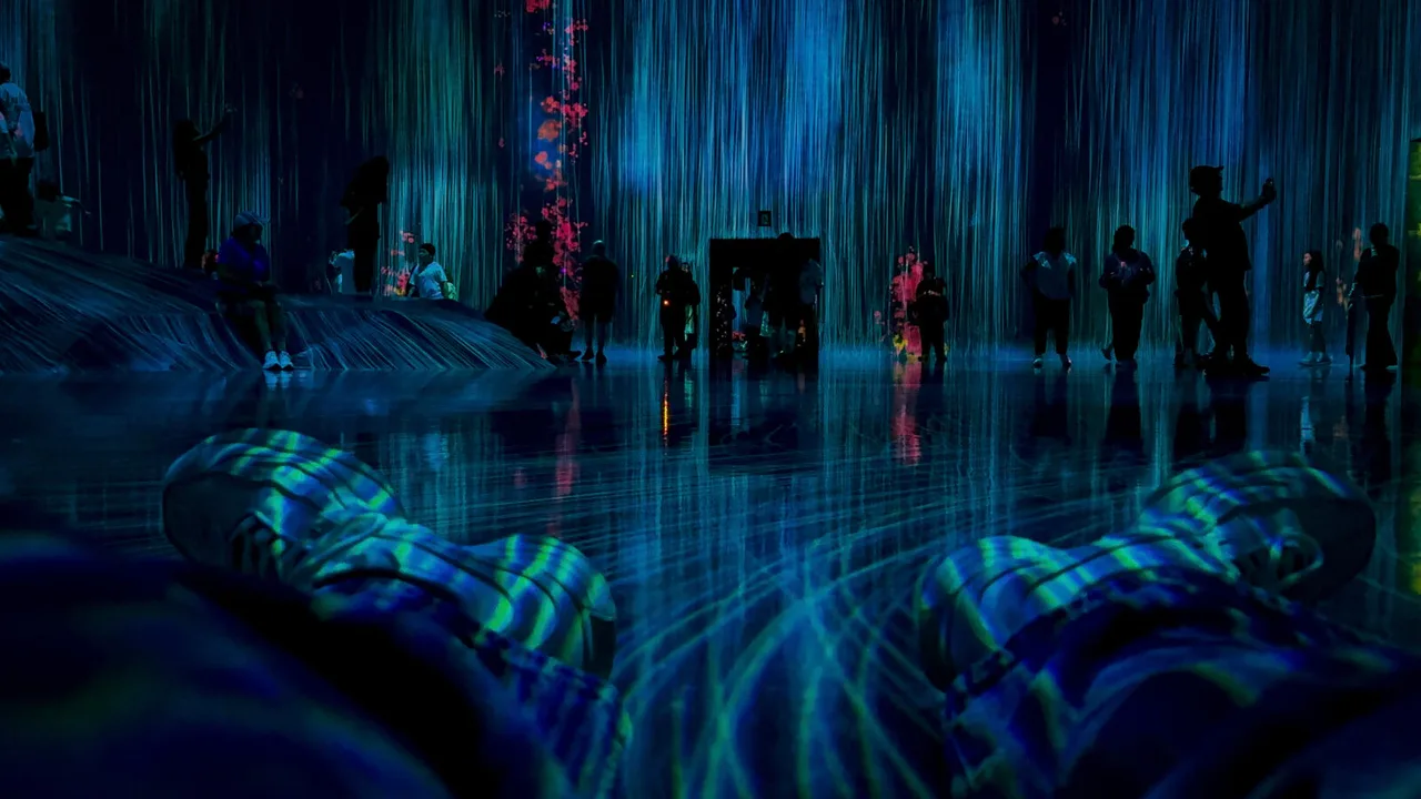 Lying on a mirrored floor in a dark room where blue light falls like rain: visitors stand in silhouette, and the photographer’s own sneakers, striped with light, fill the foreground.