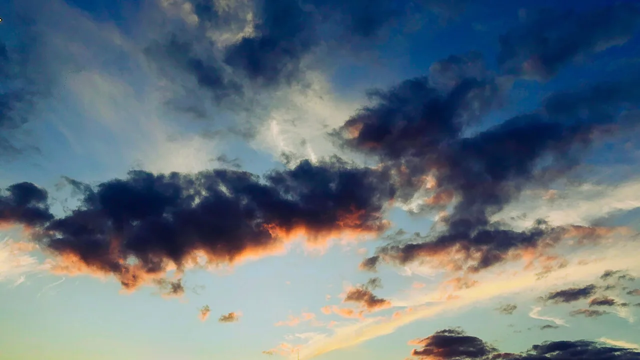 Dark clouds edged in orange by the setting sun, scattered across a deep blue evening sky.